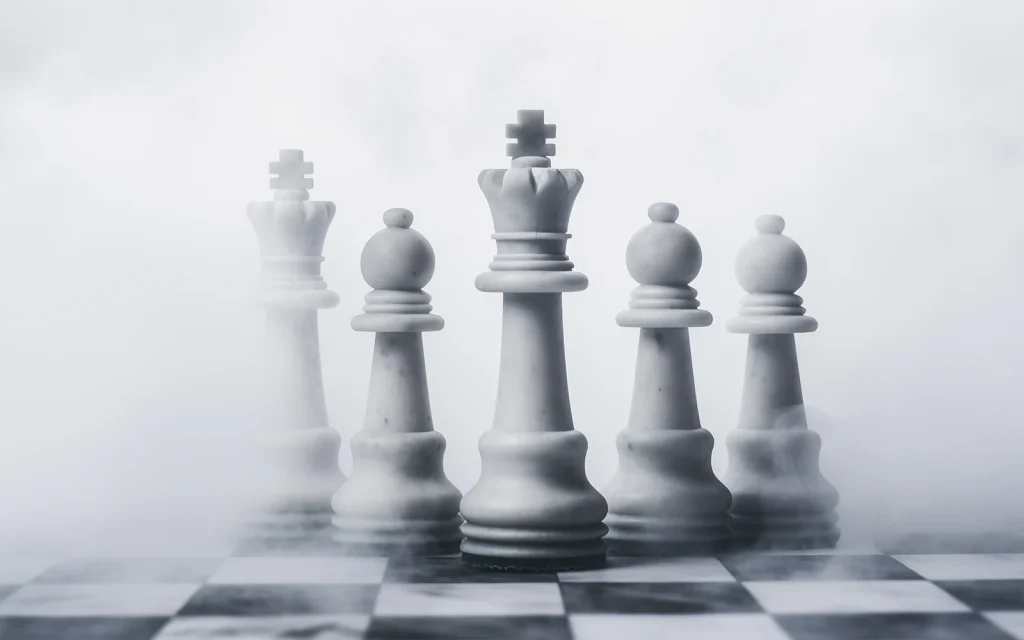 Five white marble chess pieces — kings, queens and bishops — standing on a board enveloped in atmospheric white mist.