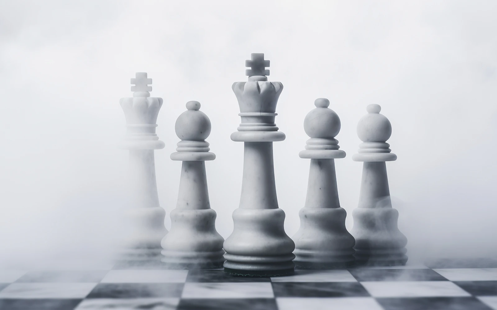 Five white marble chess pieces — kings, queens and bishops — standing on a board enveloped in atmospheric white mist.